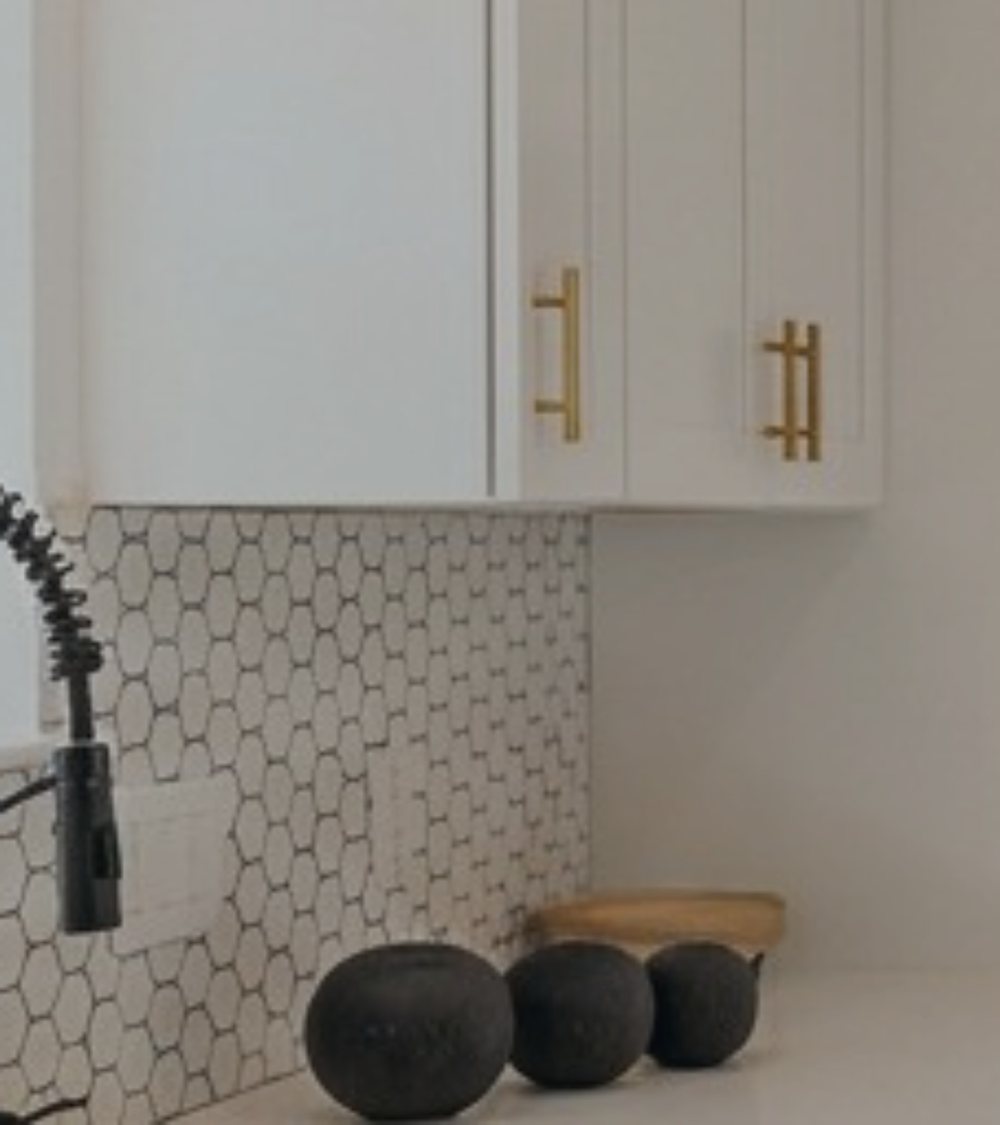 Kitchen detail with white cabinetry, brass pulls and hex tile