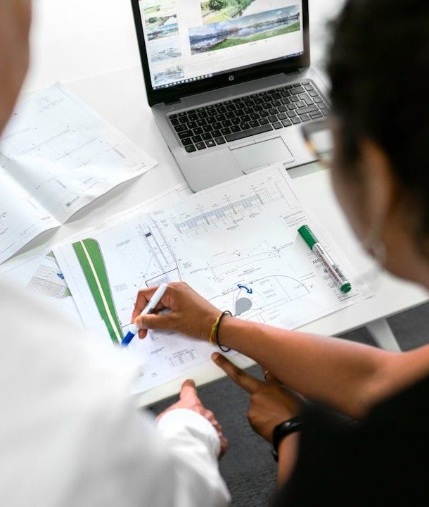 Hands marking up construction plans beside a laptop